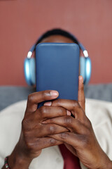 Smartphone in hands of young unrecognizable African American man in headphones relaxing in front of camera while watching video