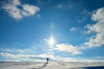 Lonely backpacker trekking in mountains choosing route in winter, sun shining bright on blue sky