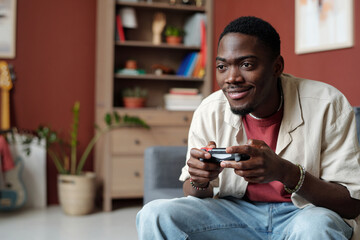 Smiling African American guy pressing buttons on controllers and looking at screen of computer or...