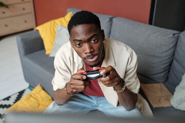 Tense African American man with gamepad in hands looking at screen of computer during video game...