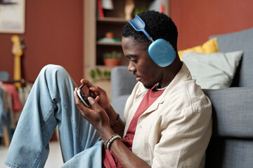 Young male gamer with smartphone connected to gamepad looking at screen while playing video game at...