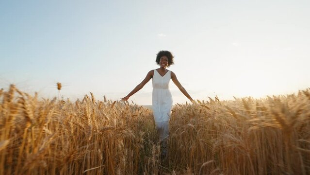 Travel concept. Graceful black woman afro hair runs in white dress across field of golden wheat towards wind smiling rejoices on walk in summer at sunset blue sky slow motion.  Go Everywhere. Freedom