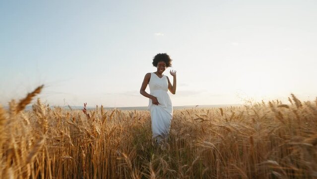 Travel concept. Graceful black woman afro hair runs in white dress across field of golden wheat towards wind smiling rejoices on walk in summer at sunset blue sky slow motion.  Go Everywhere. Freedom