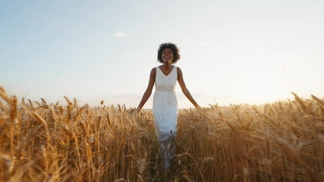 Travel concept. Graceful black woman afro hair runs in white dress across field of golden wheat towards wind smiling rejoices on walk in summer at sunset blue sky slow motion.  Go Everywhere. Freedom
