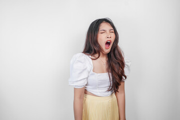 Portrait of sleepy attractive Asian woman wearing a dress, feeling tired after night without sleep, yawning with her mouth wide open