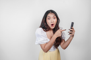 A shocked Asian woman with her mouth wide open while holding her smartphone, isolated by white background.