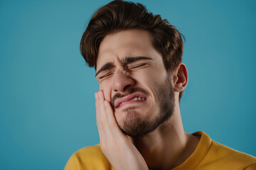 Fototapeta premium Man suffering from toothache presses his cheek shows pain and discomfort on blue background close up
