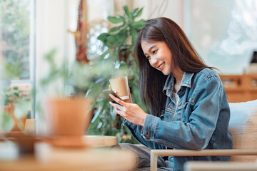 Happy Young Asian beautiful woman using smart phone and drinking coffee in the cafe