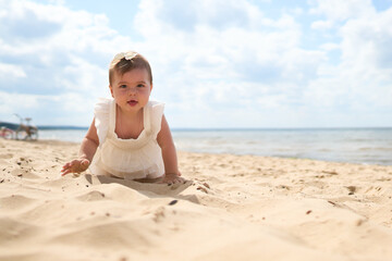 Fototapeta na wymiar A portrait of a 1 year old caucasian baby girl on the sandy beach on a sunny warm day at Baltic Sea