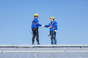 Engineers with handshake gesture on solar panels against blue sky