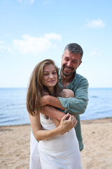 A closeup of a happy caucasian pair, the man hugging a woman from behind, Baltic sea