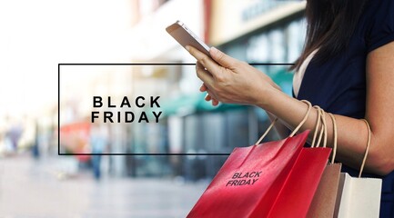 Black Friday, Woman using smartphone and holding shopping bag while standing on the mall background