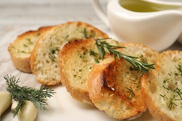 Tasty baguette with garlic, dill, rosemary and oil on board, closeup