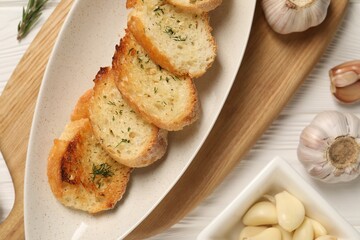 Tasty baguette with garlic and dill on white wooden table, flat lay