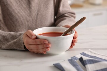 Woman eating tasty tomato soup at white marble table, closeup