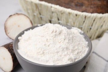 Fototapeta na wymiar Bowl with cassava flour and roots on table, closeup