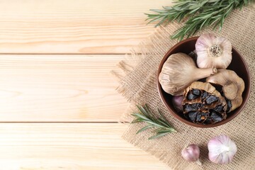 Bulbs of fresh and fermented black garlic on wooden table, flat lay. Space for text