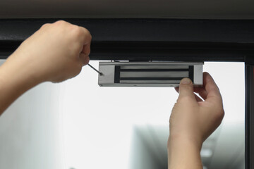 Man with screwdriver installing electromagnetic door lock indoors, closeup. Home security