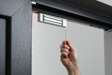 Man with screwdriver installing electromagnetic door lock indoors, closeup. Home security