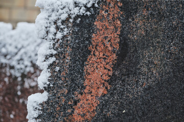 Close-up of a gray with red veins granite stone covered with snow in winter.
