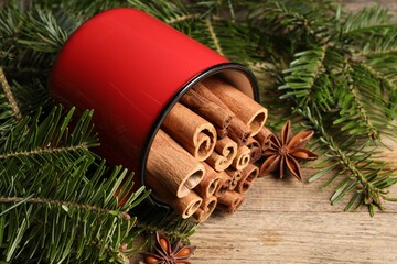 Many cinnamon sticks, anise stars and fir branches on wooden table, closeup. Aromatic spices