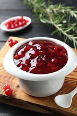 Cranberry sauce in bowl, fresh berries, spoon and rosemary on table, closeup