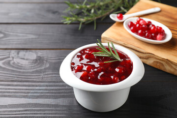 Fresh cranberry sauce in bowl and rosemary on black wooden table, closeup. Space for text