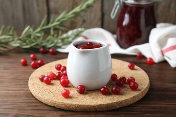 Cranberry sauce in pitcher, fresh berries and rosemary on wooden table
