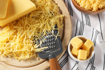 Grated, whole pieces of cheese and grater on cloth, top view