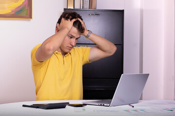 Overwhelmed at Work: Frustrated Man in Office with Laptop, Calculator, and Stress