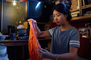 Chinese girl in grey t-shirt sitting in front of camera in microflat and looking at wet squeezed apparel of orange color