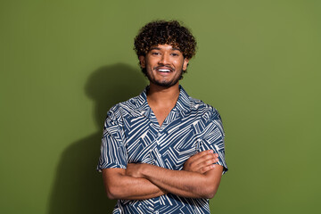 Portrait of young optimistic wavy hair hispanic guy in tropical shirt folded arms and smiling feels...