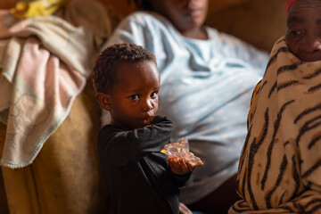 village african boy eating a snack in the room together with his mom and granny
