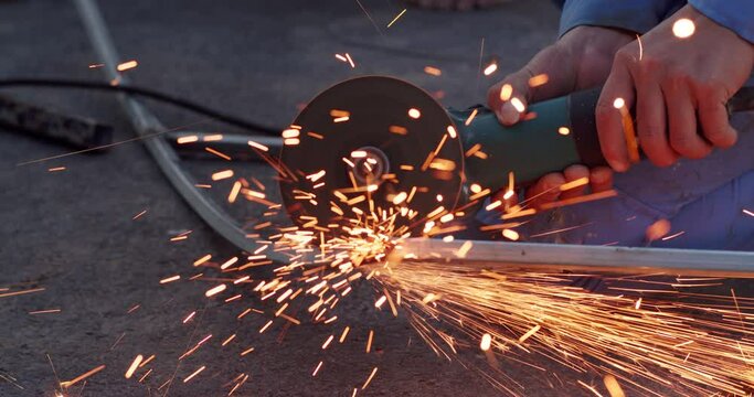 Blacksmith performing welding repair work using professional equipment. Blacksmith cutting metal using angle grinder while working in industrial workshop, man cuts rusty metal beam using round turbine
