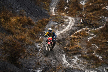 Professional motorcyclist in full moto equipment riding crops enduro bike in mountains, enduro driver rides through mud and puddles in the rain, motorcycle race