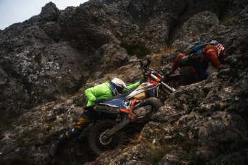 Two professional motorcyclist in full moto equipment riding crops enduro bike, concept of epic rock motocross race, help at the race competition