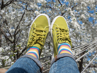 Trendy sneakers and colorful socks on the background of flowering trees. Closeup, outdoors. Men's and women's fashion style. Beauty and elegance concept