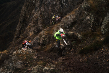 Epic scene of motocross racing in the rocky mountains in rainy weather, the racer lifts the...