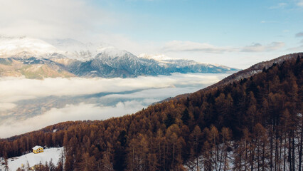 Aerial view of winter landscape with mountain peaks covered with snow, fluffy clouds and coniferous forest. Natural background.