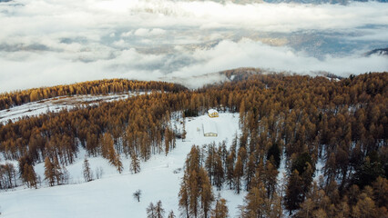 Aerial view of winter landscape with mountain slopes covered with snow, fluffy clouds and coniferous forest. Natural background.