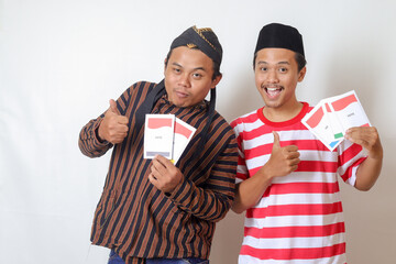 Portrait of two excited Indonesian man from Javanese and Madurese tribes holding voting paper for General Election (Pemilu) of president and government of Indonesia. Isolated image on gray background - obrazy, fototapety, plakaty