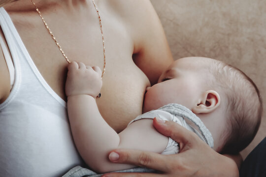 Close up young mom breastfeeding newborn baby at home. Woman nursing baby in bedroom. Care mother spends her time caring for newborn child. Concept of motherhood and happy family. Copy space