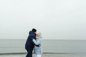 An elderly couple is having fun and dancing on the beach by the sea in winter.
