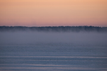 Sea winter landscape at sunrise, steam from the water.