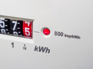 A close-up of an electric meter with flashing red LED light, energy consumption and red dial number 5. Concept meter reading, electricity prices, bills, cost of living, fuel and heating costs.
