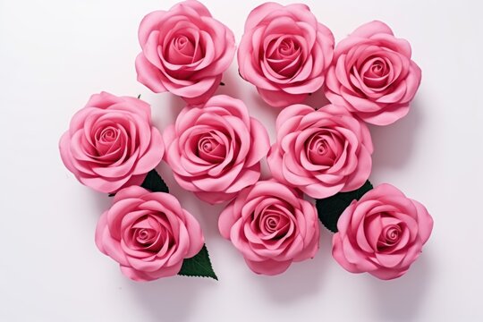  a bunch of pink roses sitting on top of a white table next to a green leafy plant in the center of the picture, on a white background is a white surface.