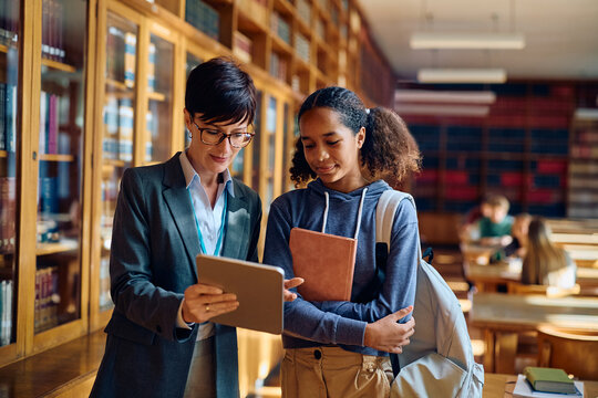 Black high school student and her teacher using digital tablet in classroom.