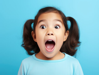 Surprised little girl with open mouth on a blue background.