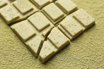 Pieces of tasty matcha chocolate bar on green powder, closeup