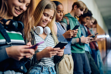 Happy teenage girl and her classmates using smart phones at high school.
